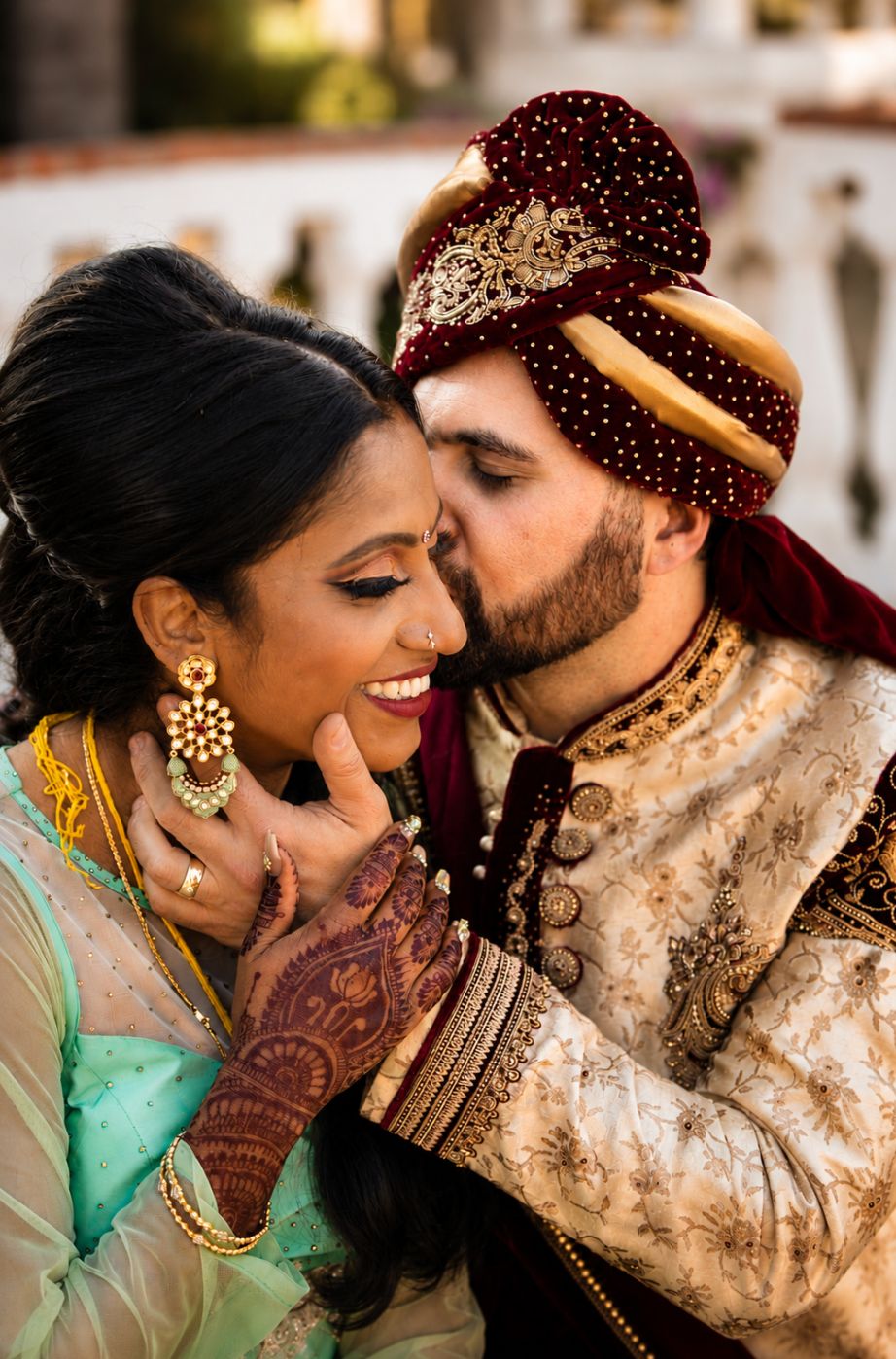 Groom in a maroon and gold turban kissing his bride's cheek at an Indian wedding in Southern California — wedding photography by Murrieta Media